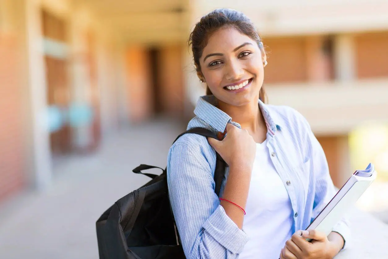A woman is smiling while holding her backpack.